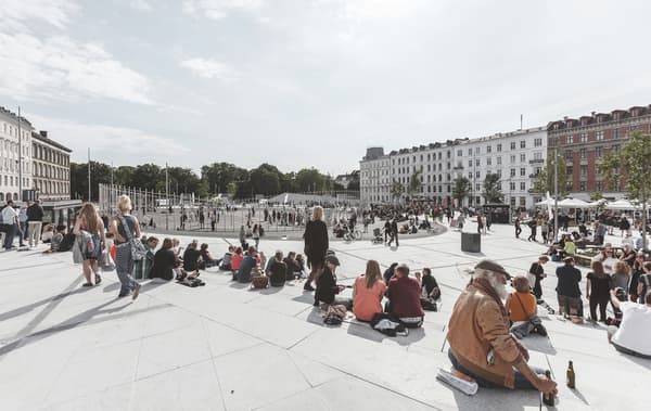 Grande place ouverte avec de nombreuses personnes, des stands sur les côtés et une aire de sport au centre.
