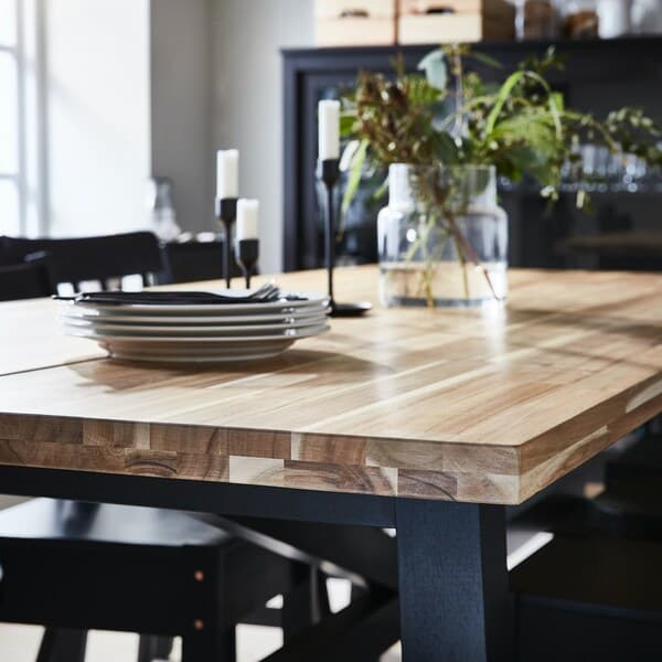 Grande table à manger en bois avec des assiettes empilées, deux bougeoires et une vase en verre transparent.