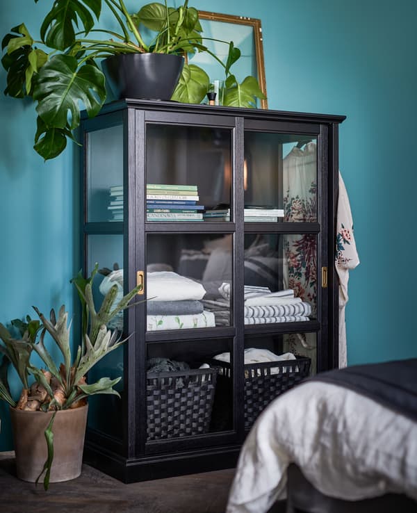 Grande vitrine entourée de plantes vertes et remplie de livres et de linge de lit.