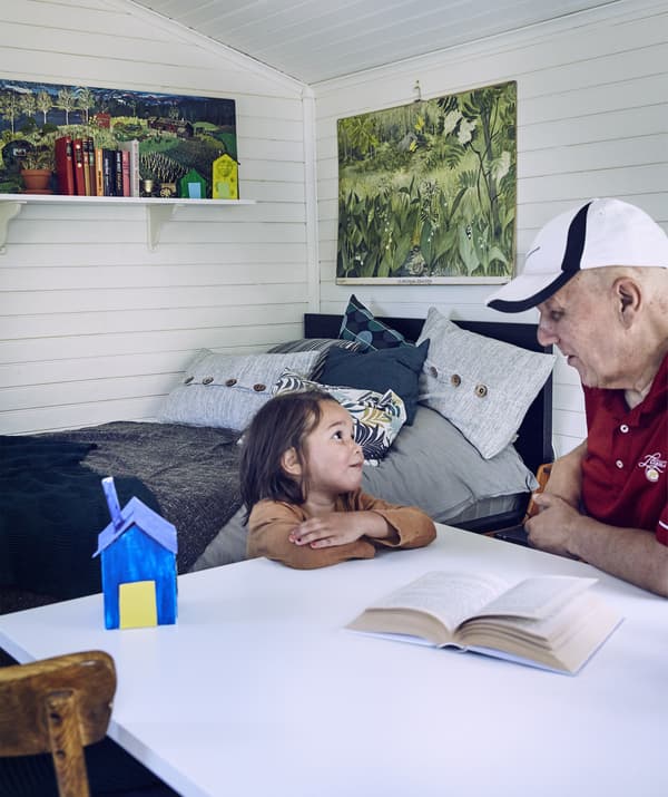 Grandpa and grandson sitting at a fold-out table in a self-contained annex room with white-washed wooden walls and wall art.