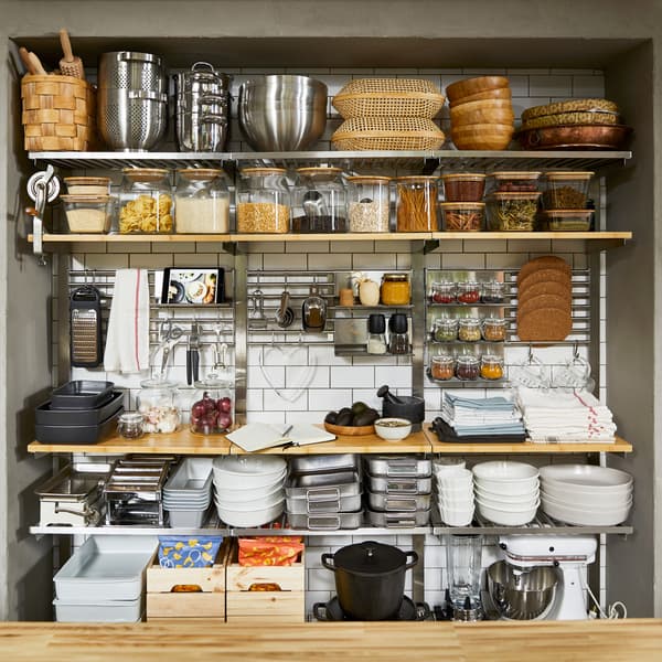 Grands rangements muraux avec étagères et grilles en bois/inox. On y voit des ustensiles de cuisine et de la nourriture.