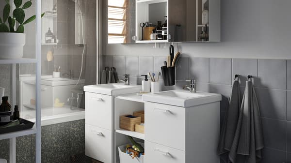 Graues Badezimmer mit Waschkommode/Waschbecken in der Mitte, einem Schrank mit Spiegeltüren sowie Handtüchern in Grau.