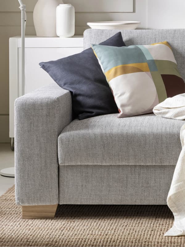 Gray sofa with blue and colorful cushion, white cabinet with decor in background