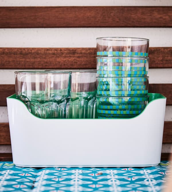 Green and patterned cups stacked in an open plastic container on a table.