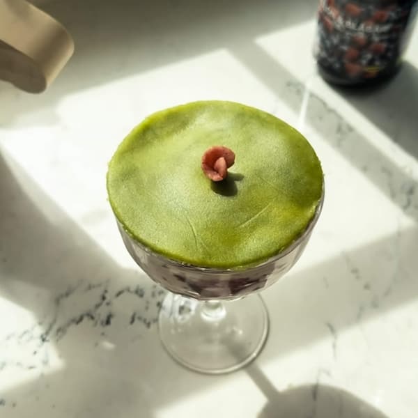 Green and pink dessert in a glass, topped with smooth green foam and a small garnish.

