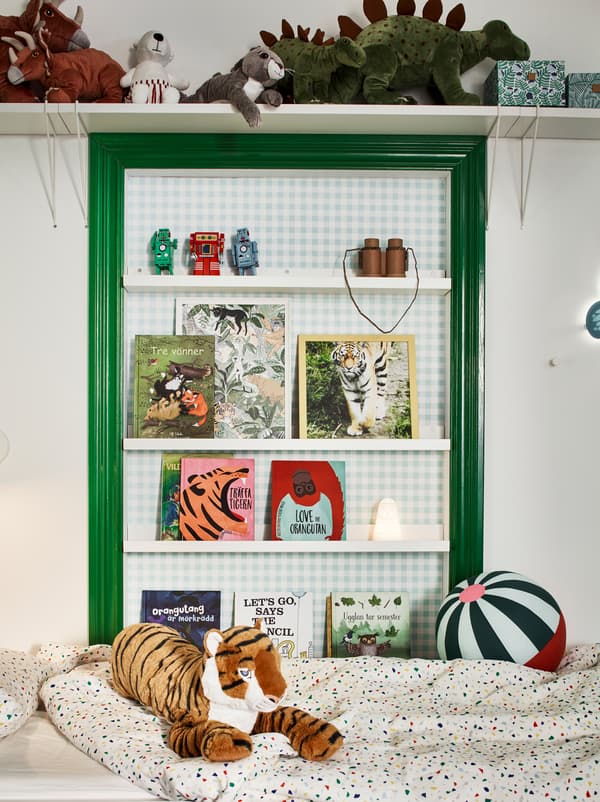 Green and white wall above the bed in a children’s room. Soft toys on a wall shelf and books on MOSSLANDA picture ledges.