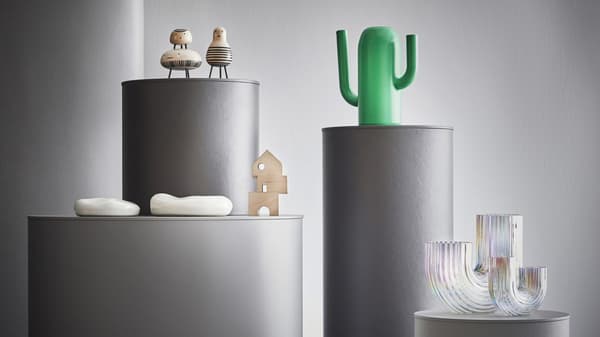 Green cactus shaped watering can on platform with small decor figures on platforms