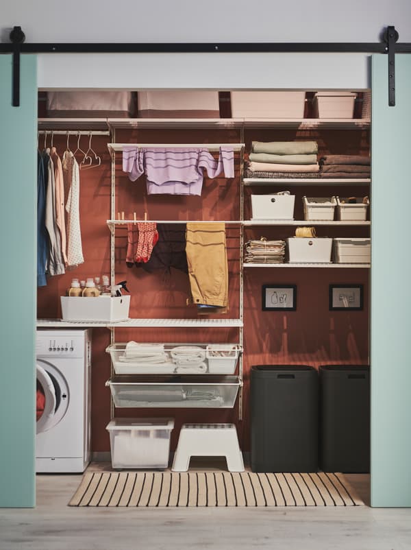 Green doors slid open to reveal a wall arranged for laundry, including GIGANTISK bins, BOAXEL shelving and a washing machine.