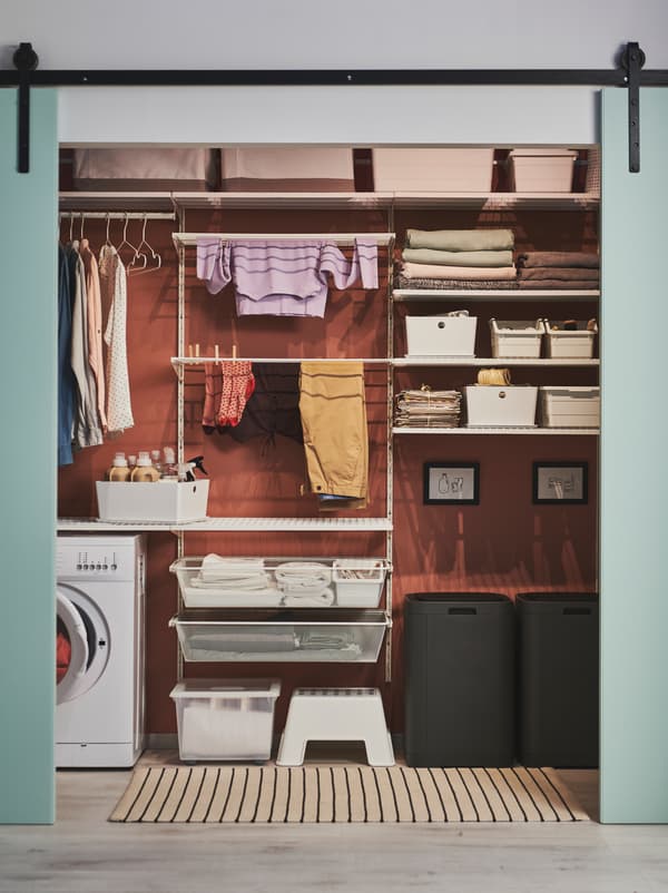 Green doors slid open to reveal a wall arranged for laundry, including GIGANTISK bins, BOAXEL shelving and a washing machine.