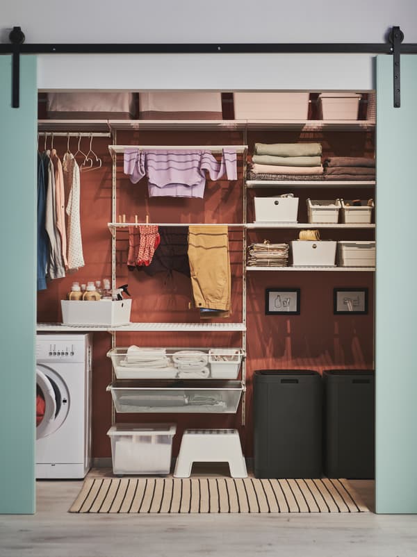 Green doors slid open to reveal a wall arranged for laundry, including GIGANTISK bins, BOAXEL shelving and a washing machine.