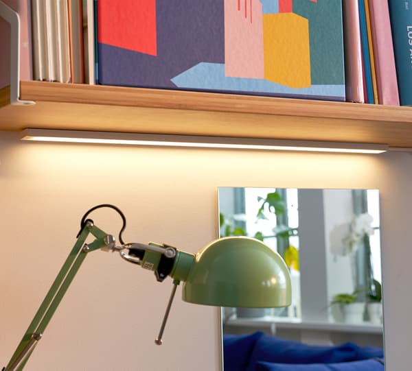 Green OMLOPP LED worktop lighting, with a mirror behind it reflecting the room and a shelf above filled with colourful items.