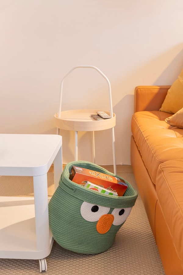 Green owl-shaped storage basket with board games near sofa.