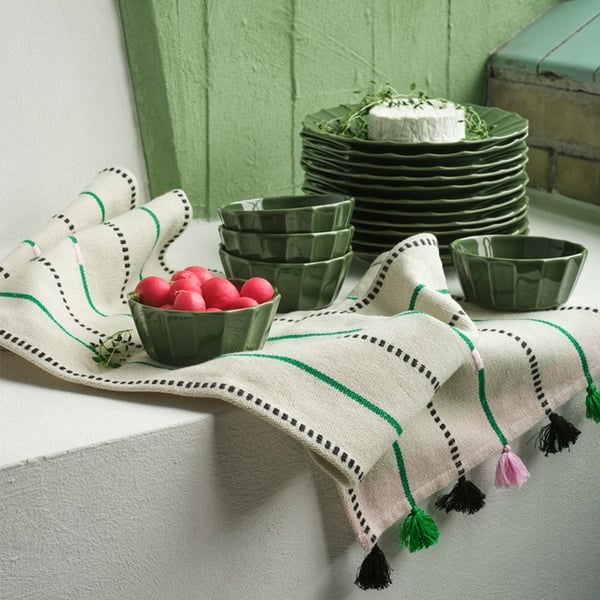Green plates and bowls are displayed on a beige-green rug from the MÄVINN collection.