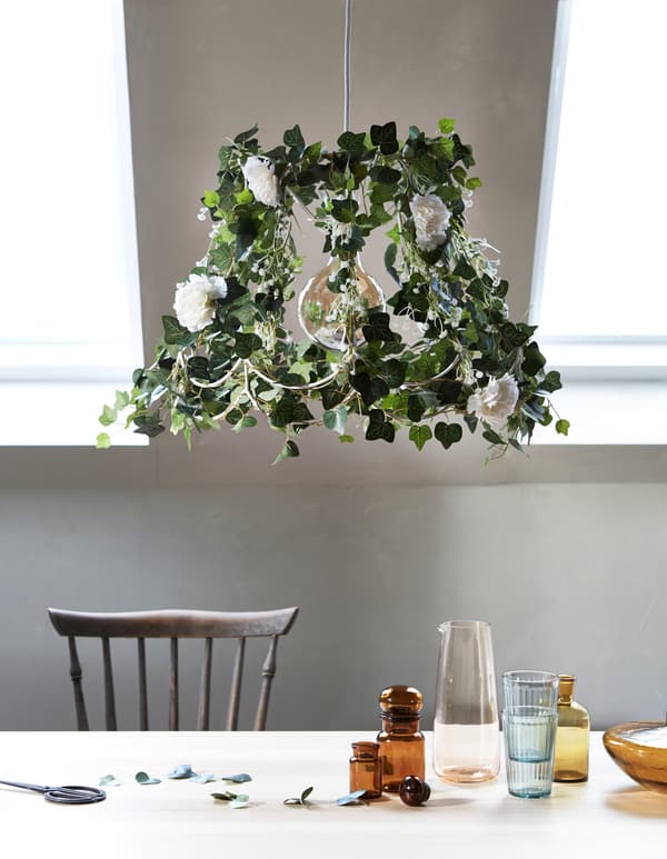 Greenery in the home, made by updating an old lamp with artificial flowers and green plants, with a table in the foreground.