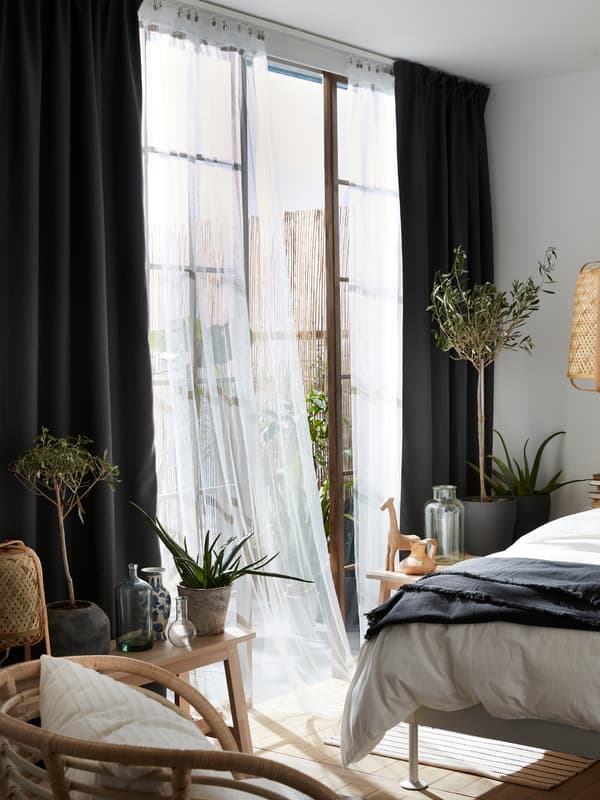 Grey ANNAKAJSA room darkening curtains combined with sheer white curtains, a BUSKBO armchair and olive trees in pots.