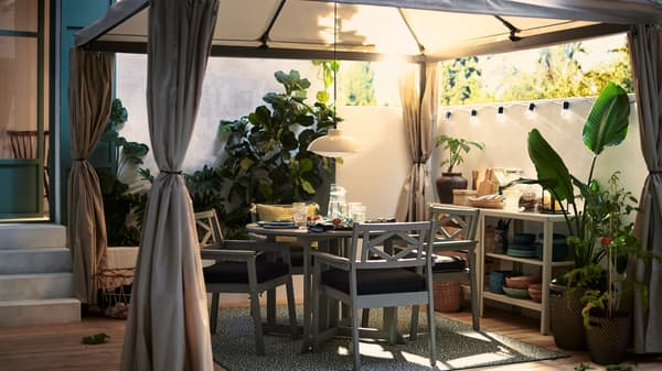 Grey BONDHOLMEN outdoor dining table and chairs for four people to enjoy dinner outside on the deck under a fabric gazebo.