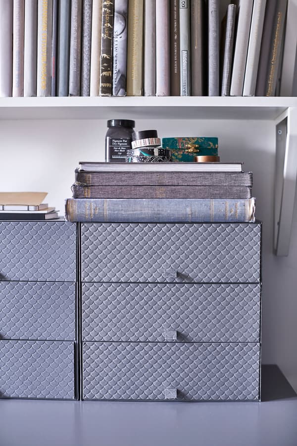 Grey boxes with drawers on a desk in a bedroom.