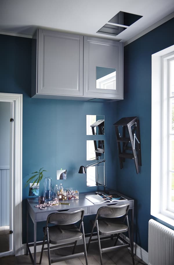 Grey closed cupboards placed right up at the ceiling next to a dining area in a bright blue room.
