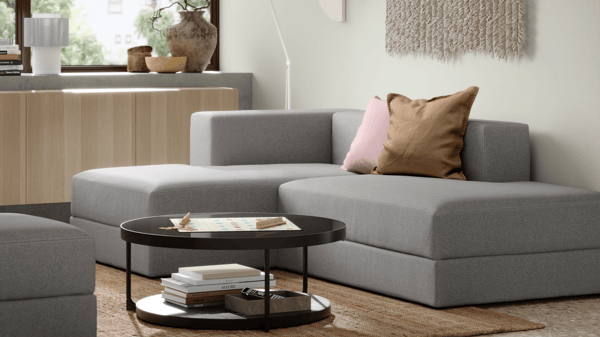 Grey JÄTTEBO modular sofa with chaise lounge in a minimalist space, complemented by neutral decor and a black round coffee table with books.