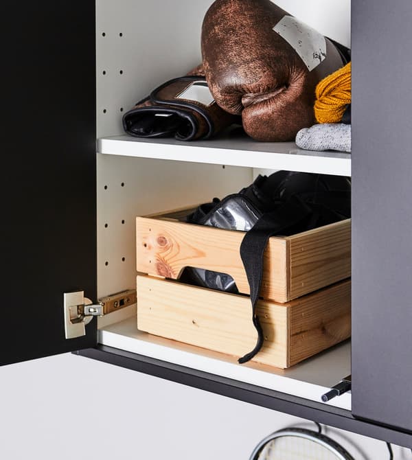 Grijze kast met twee deuren staat half open, zodat we twee witte legplanken zien met daarop bokshandschoenen en uitrusting in een grenen kistje.