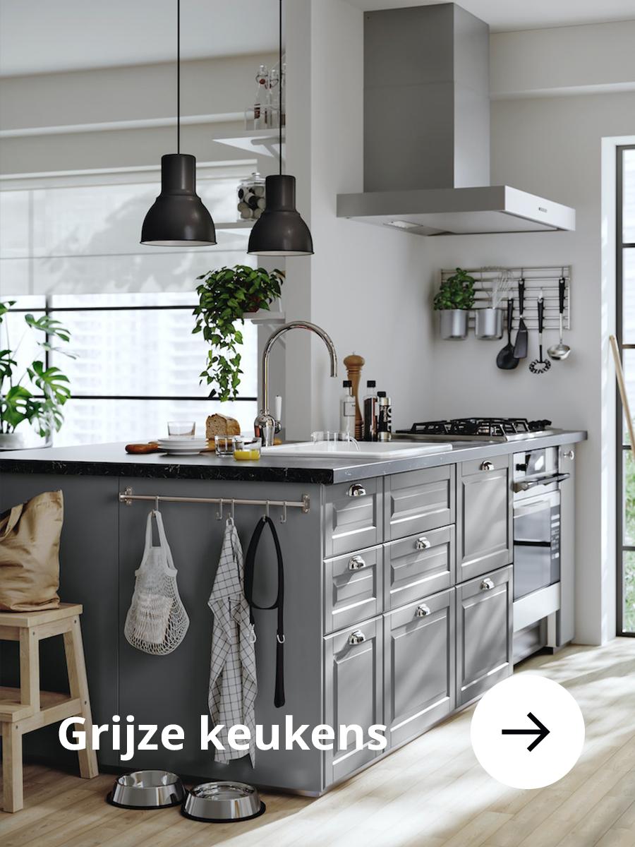 Grijze keuken met een donker aanrechtblad en twee zwarte hanglampen aan het plafond.