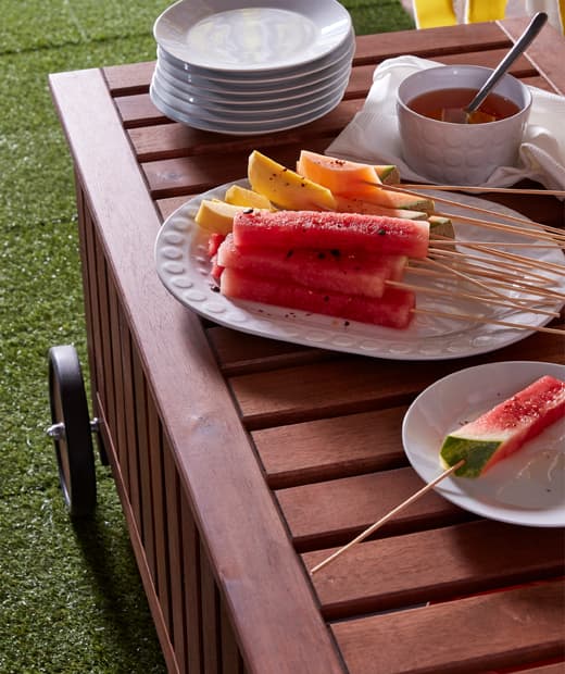 แตงโมและมะม่วงหั่นเป็นชิ้นเสียบด้วยไม้ไผ่ปลายแหลม GRILLTIDER ของอิเกียบนจานใหญ่สีขาว