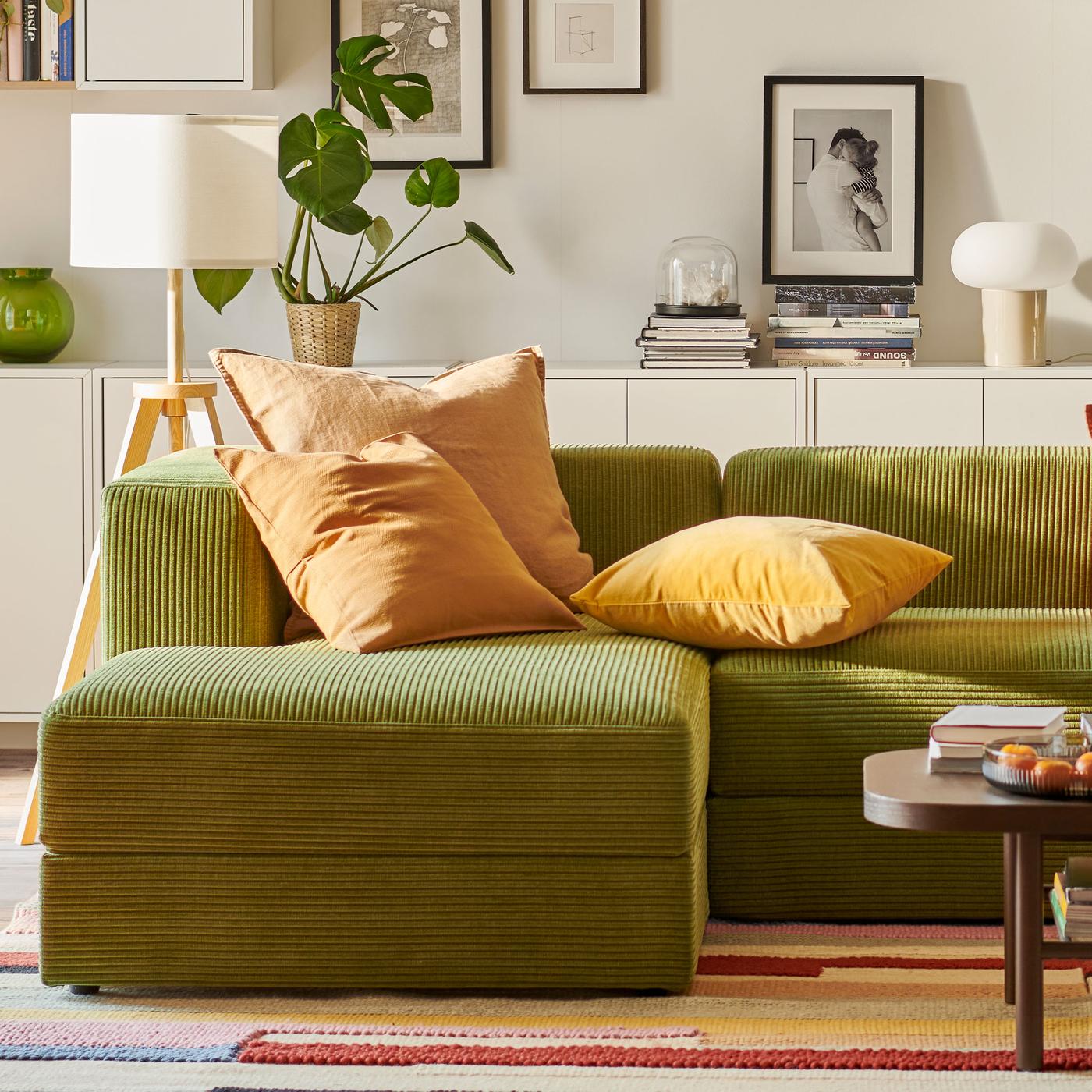 Grön JÄTTEBO manchestersoffa i vitt vardagsrum med färgglad matta och orangea kuddar.