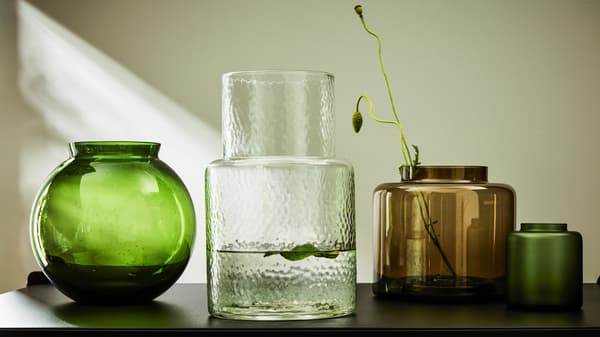 Groene, helderglazen, bruine en matgroene KONSTFULL vazen staan op een houten buffetkast, terwijl het licht naar binnen schijnt.