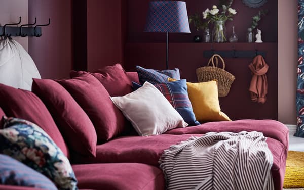 GRÖNLID كنبة حمراء داكنة من ايكيا مع أريكتي استرخاء طويلتين بجانب بعضهما البعض، عليها وسائد SANELA وردية وصفراء.