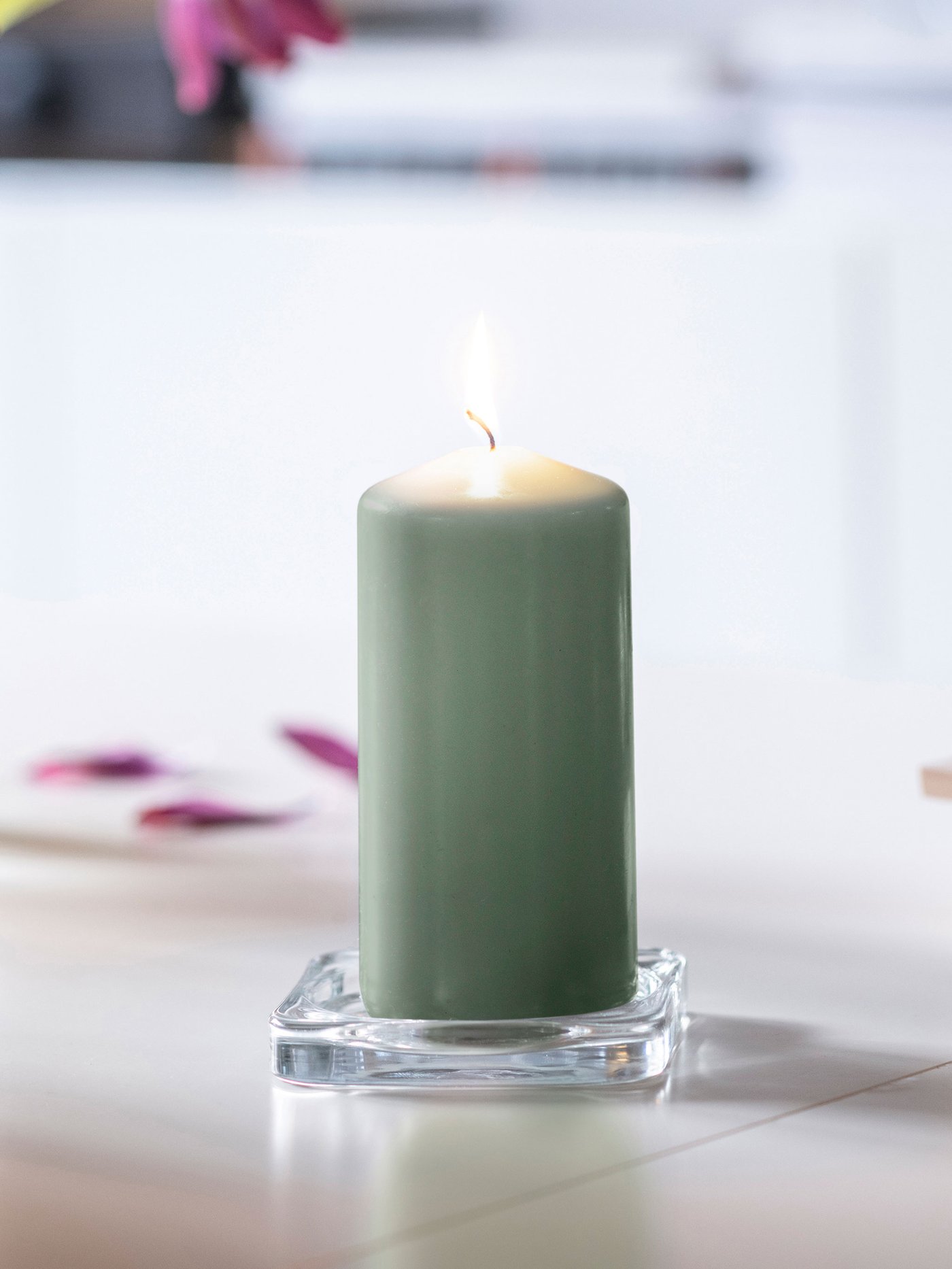 Grönt blockljus som brinner, stående på en vit yta med mjuk bakgrund.