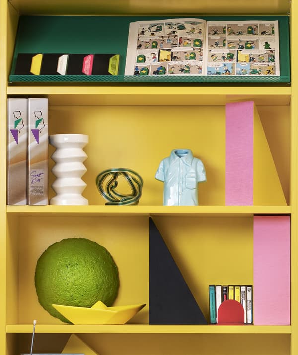 Gros plan de deux tablettes d’une bibliothèque jaune vif ornées d’objets décoratifs.