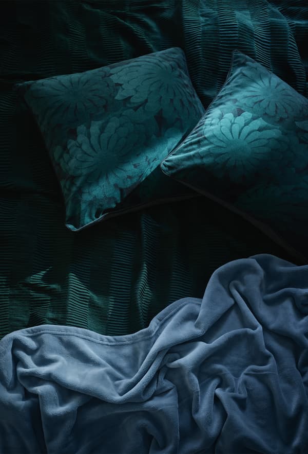 Gros plan de linge de lit et de coussins vert foncé et bleus.