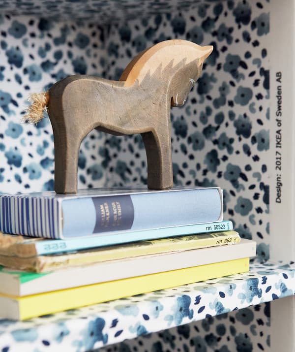 Gros plan de livres et d’un cheval comme objet de décoration sur une étagère au motif floral bleu.