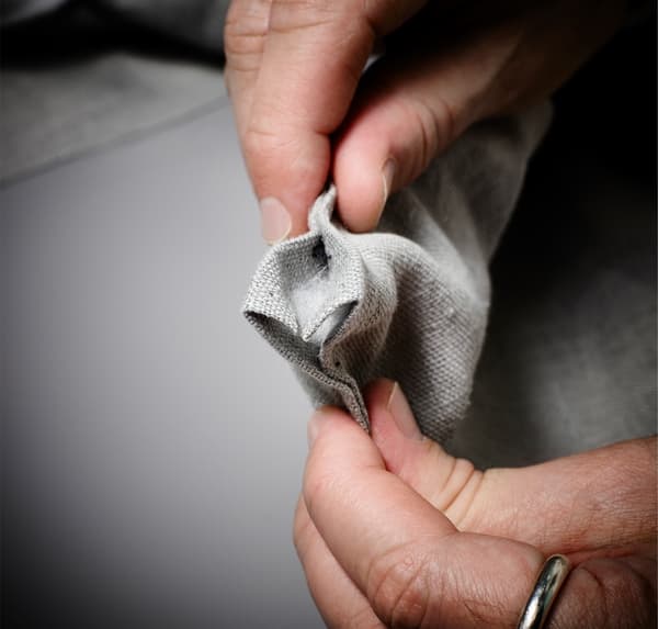 Gros plan de mains, montrant comment épingler l’ourlet en place sur un tissu gris.