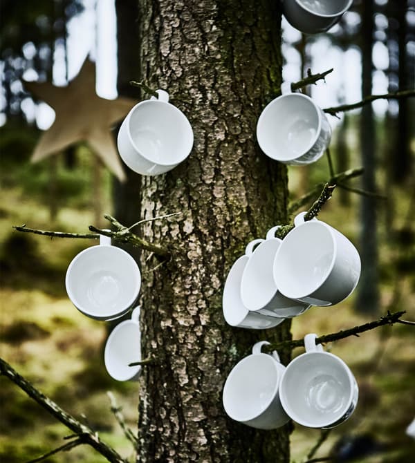 Gros plan de tasses de café blanches accrochées à de petites branches dans le cadre d’un repas de noces en forêt