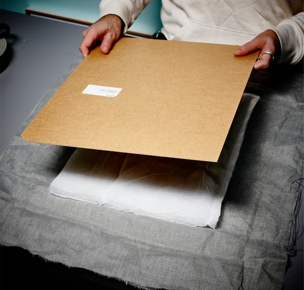 Gros plan des mains d’une personne superposant du tissu gris et de l’ouate blanche sur le dos d’un cadre.