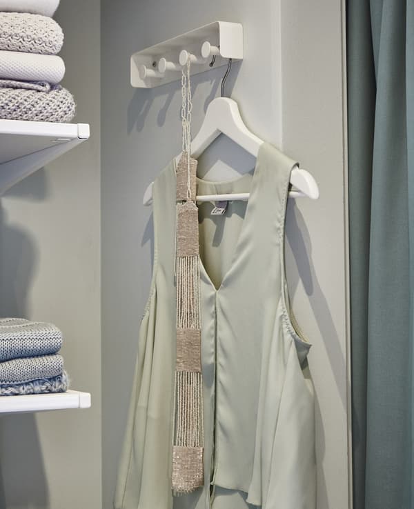 Gros plan du porte-serviettes blanc ENUDDDEN utilisé comme lieu de stockage pour la tenue du lendemain, un haut vert clair avec une ceinture.