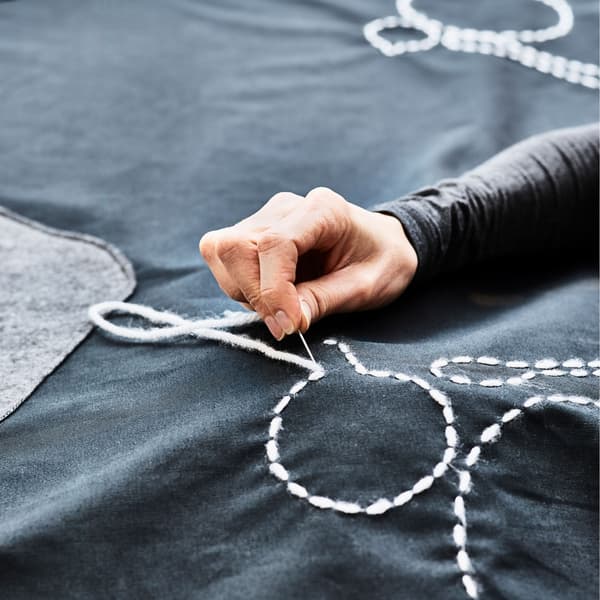 Gros plan d’un contour d’assiette cousu sur une nappe et GIF animé montrant une table d’extérieur en train d’être couverte d’une nappe ressemblant à un tapis de jeu avec des routes