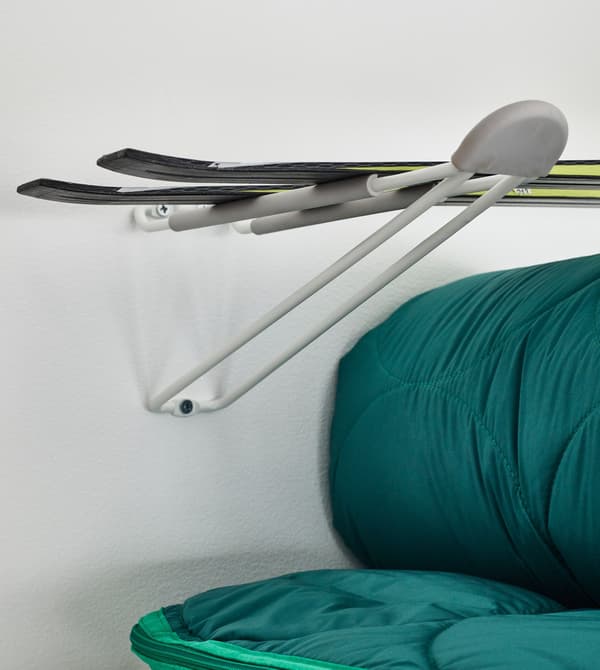 Gros plan d’un grand crochet fixé au mur pour supporter une paire de skis, près d’un canapé.