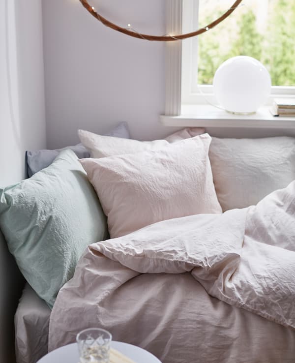 Gros plan d’un lit cosy avec linge de lit teint à la main dans des teintes pastel.