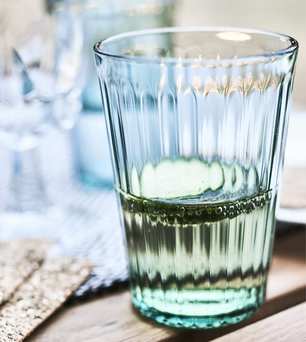 Gros plan d’un verre vert rempli de liquide et de tranches de concombre.