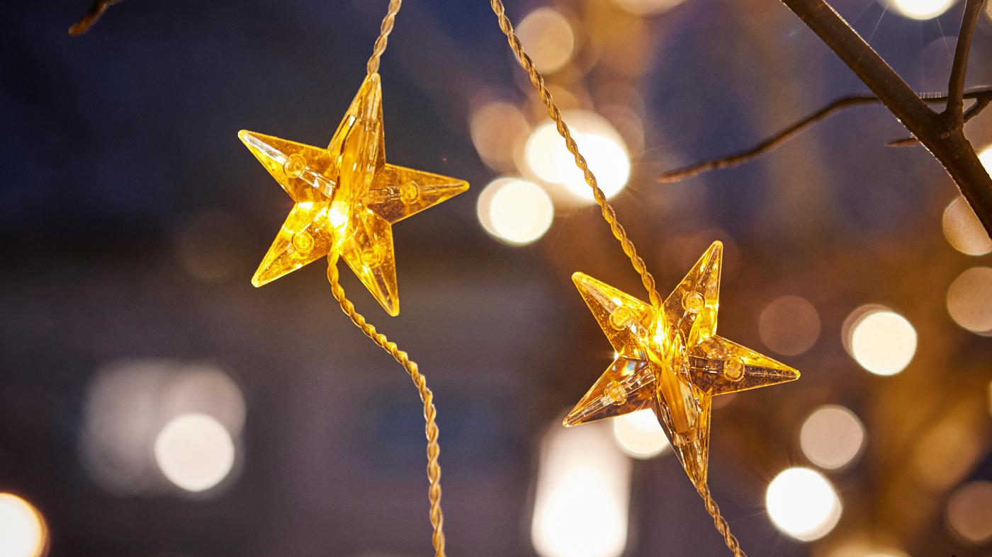 Gros plan d’une guirlande lumineuse à LED STRÅLA dorée avec lampes en étoiles ornant un arbre à l’extérieur.