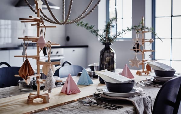 Gros plan d'une table décorée d'origami pastel, de verdure dans un vase et d'une planche en bois en guise de chemin de table.
