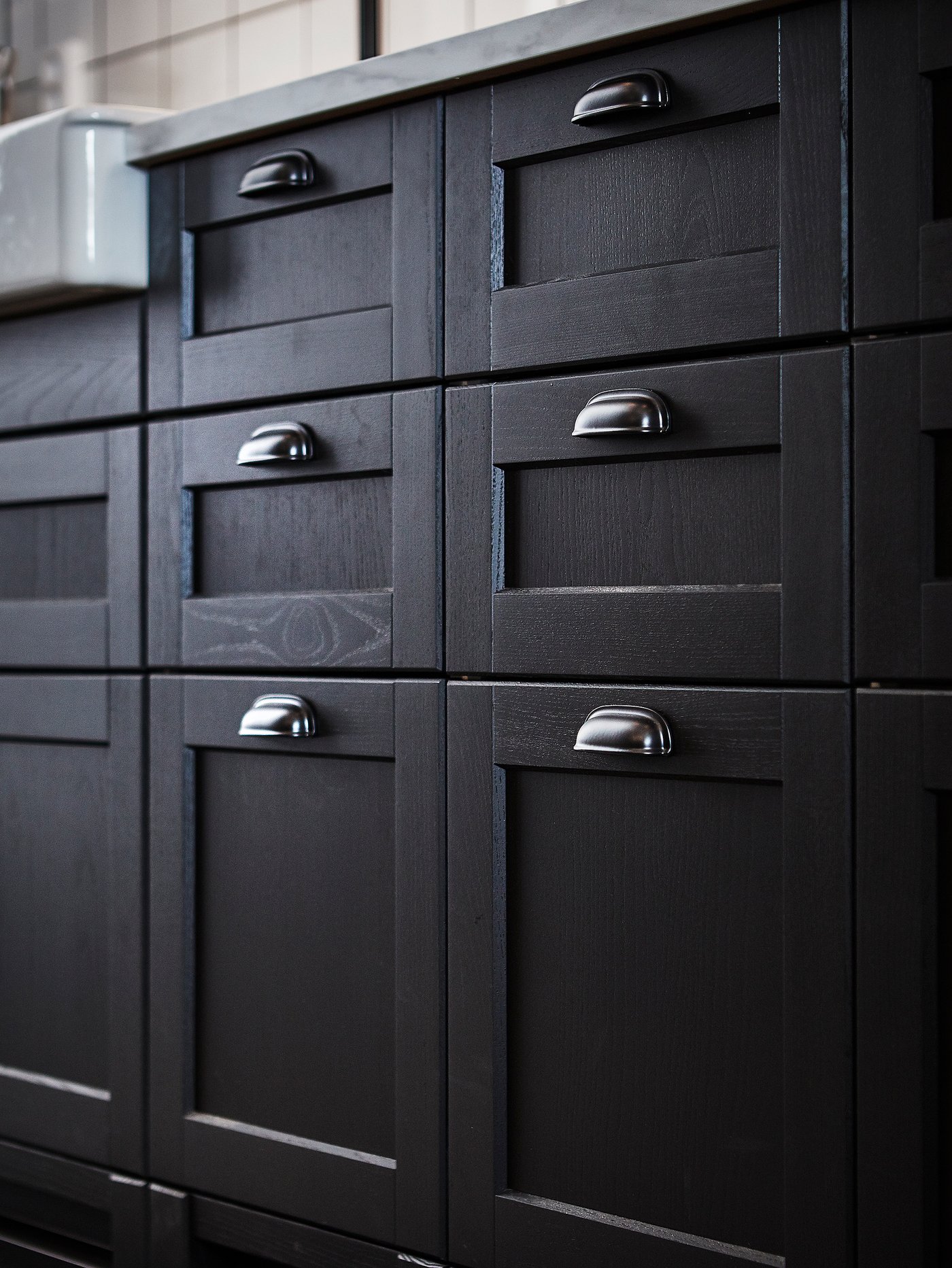 Gros plan sur des armoires de cuisine avec des façades de tiroir LERHYTTAN teintes en noir et des poignées arrondies ENERYDA.
