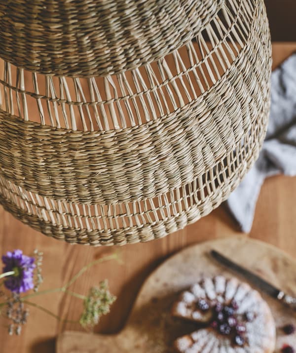 Gros-plan sur la décoration d’une suspension faite en jonc de mer naturel, suspendue au-dessus d’une table en bois.