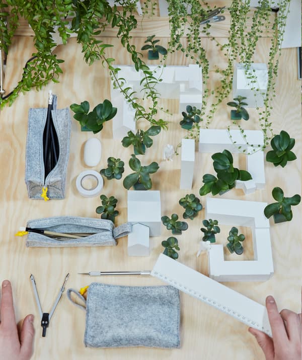 Gros plan sur le projet architectural d'un étudiant avec des immeubles entourés de verdure, un cutter et une règle.