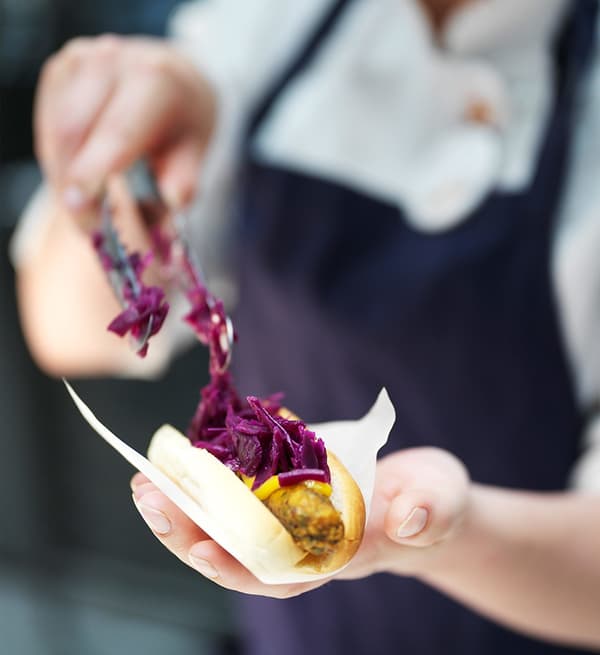 Gros plan sur un employé du bistro IKEA déposant du chou rouge sur un hot-dog végétarien IKEA, un snack à base de plantes.