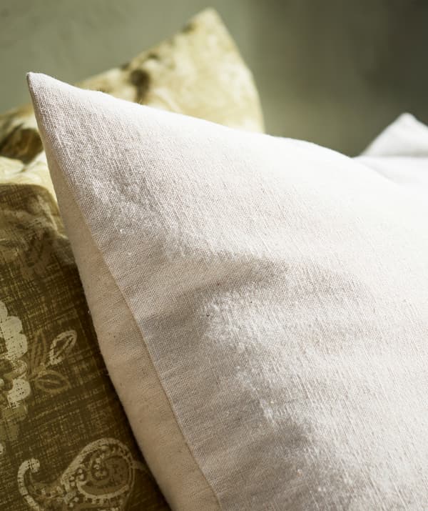 Gros plan sur un oreiller beige en coton naturel à côté d’un oreiller vert en cachemire.