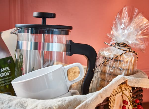 Gros plan sur un panier cadeau avec un paquet de café, une cafetière, des mugs et des biscuits à l'avoine.