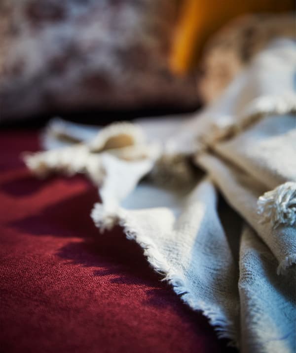 Gros plan sur un plaid JOFRID écru réalisé en coton et en lin, sur un canapé rouge.